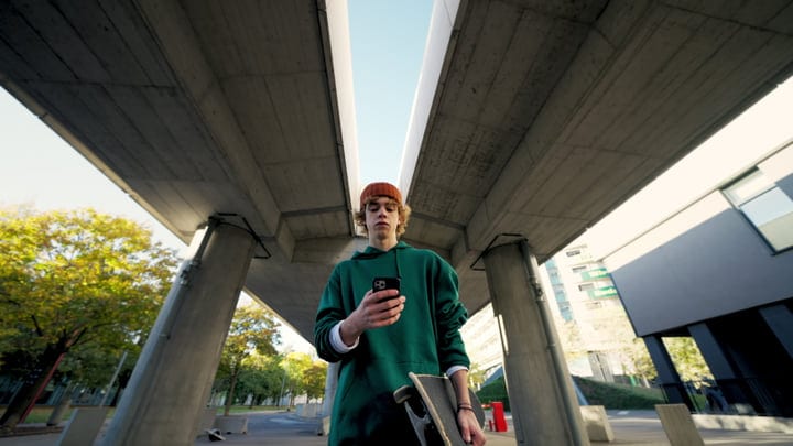 Young Skateboarder Checks Phone Under City Bridge