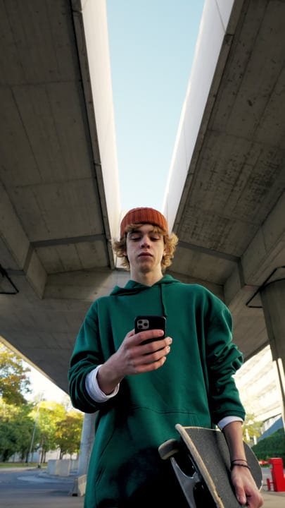 Youthful Skater Checks Phone Under Urban Bridge