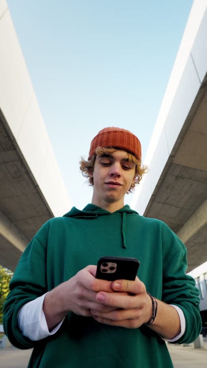 Young Man Engages with Smartphone Under Urban Overpass