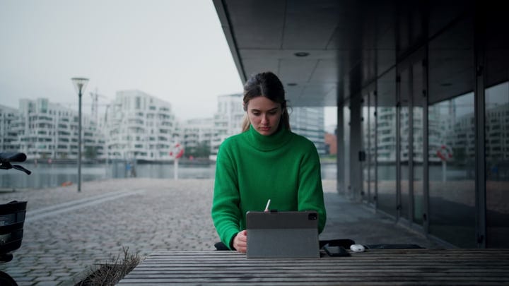 Focused Woman in Green Sweater Working by the Canal