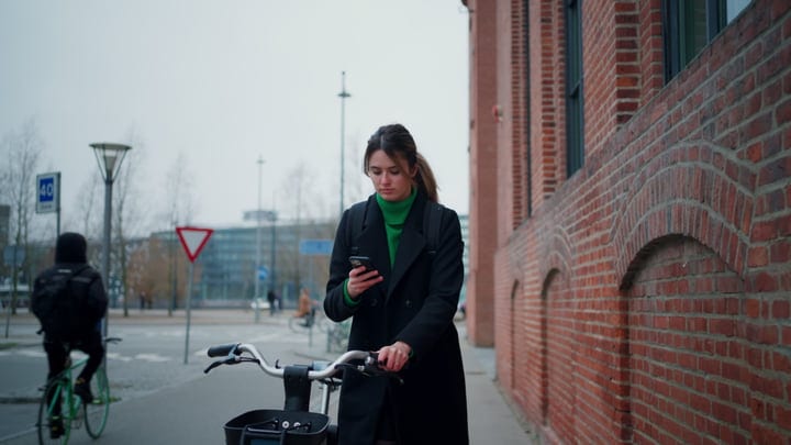 Focused Businesswoman Checks Her Phone While Cycling In Copenhagen
