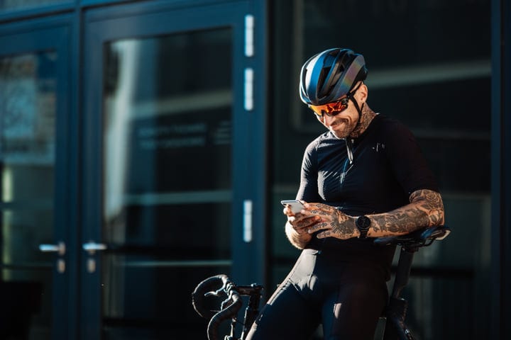 Urban Cyclist Pauses To Check Messages In City Sunlight