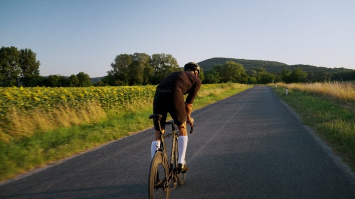 Cyclist Rides Road Bike Through Sunflower Fields At Golden Hour