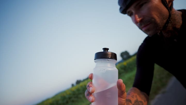 A Cyclist Pauses, Reaching For Hydration On A Sunny Ride