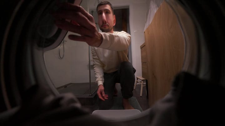 Focused Man Reaching Inside Washing Machine At Home