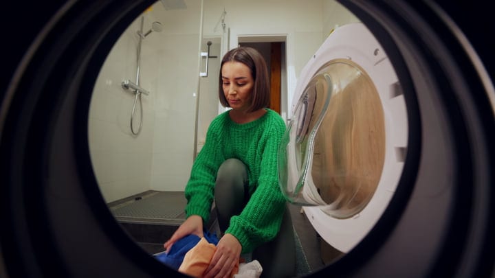Woman In Green Sweater Loads Laundry Into Washer