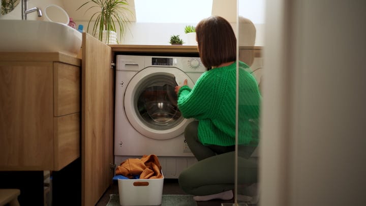 Woman in Cozy Sweater Loading Her Washing Machine