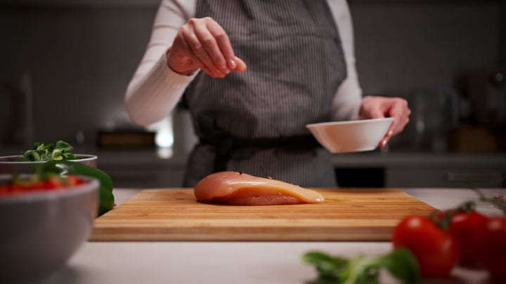 A Culinary Dance: Woman Seasoning Chicken In Her Kitchen