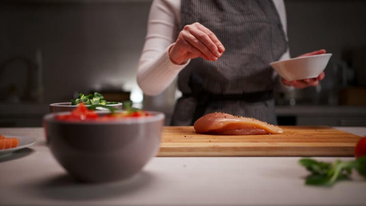 A Woman Seasons Chicken in a Contemporary Kitchen