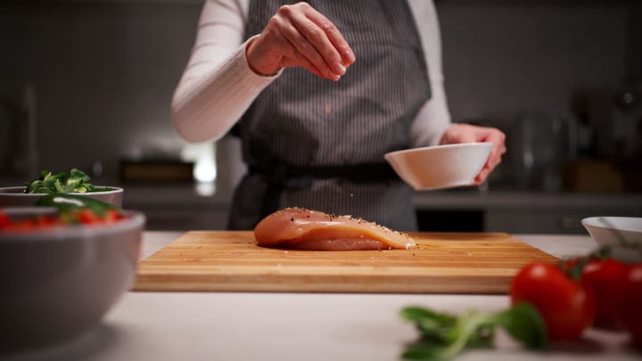 Sprinkling Spices On Chicken In A Cozy Kitchen