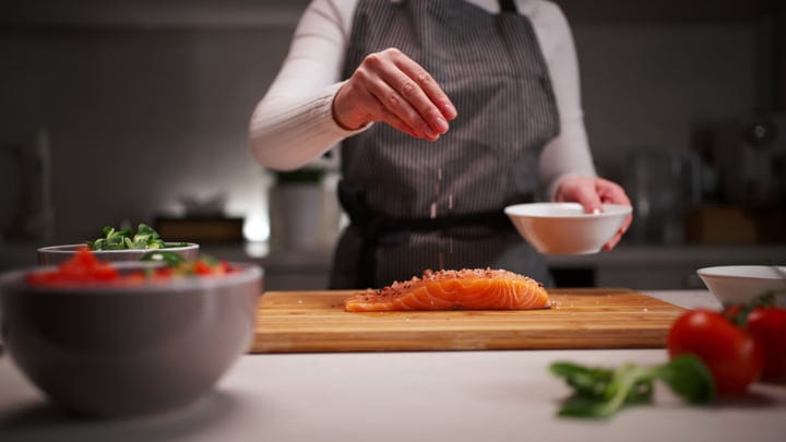 Culinary Crafting: Woman Seasoning Salmon in Modern Kitchen