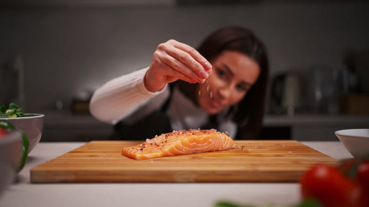 A Woman Seasons Salmon In A Cozy Kitchen Setting