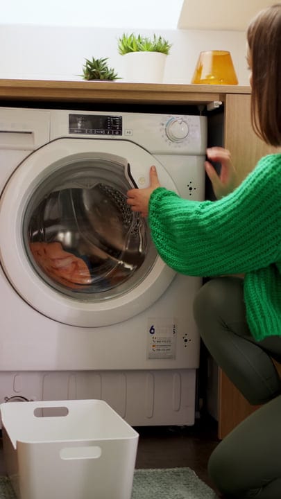 Green Sweatered Woman Loads Laundry Into Washing Machine