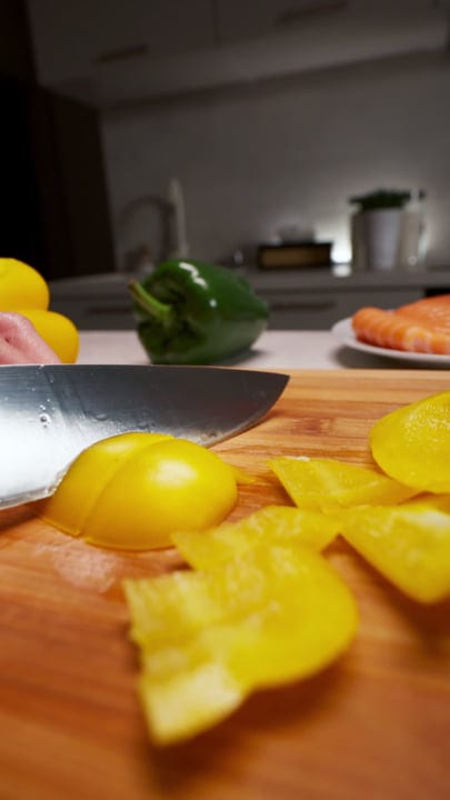 Slicing Vibrant Peppers On A Wooden Board At Home