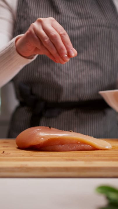 Sprinkling Spice Over Fresh Chicken In An Inviting Kitchen