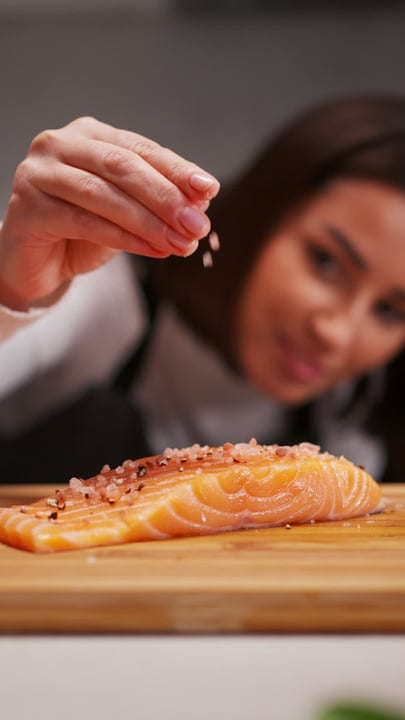 A Woman Carefully Seasons Fresh Salmon At Home