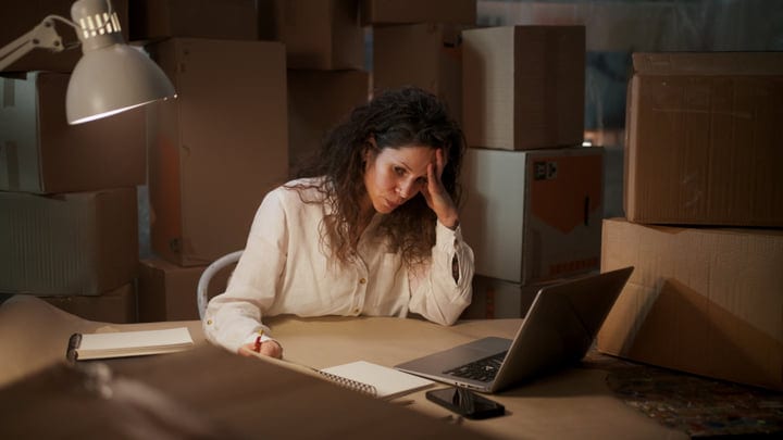 Woman Works Late On Laptop In Box-Filled Storage Room