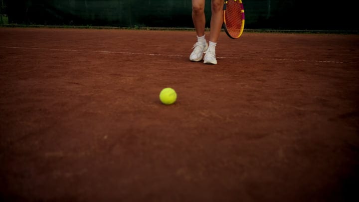 Tennis Player's Feet Standing On Red Clay Court With Ball And Racket
