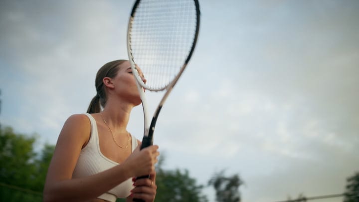 Young Woman Swings Tennis Racket To Serve On Outdoor Court