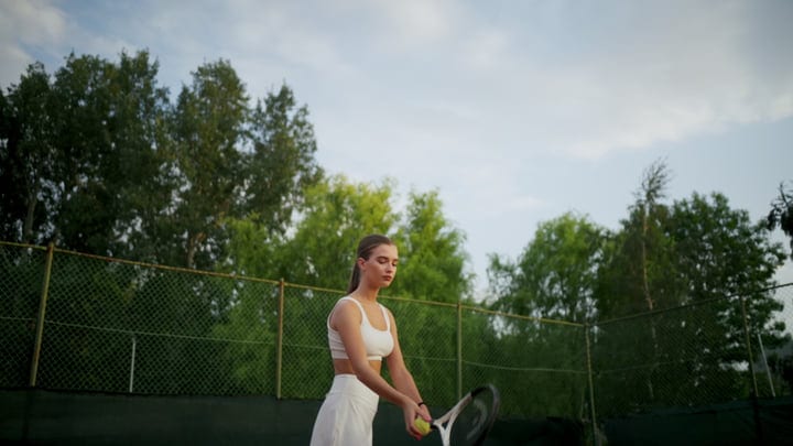 Young Woman Preparing To Serve A Tennis Ball On Outdoor Court