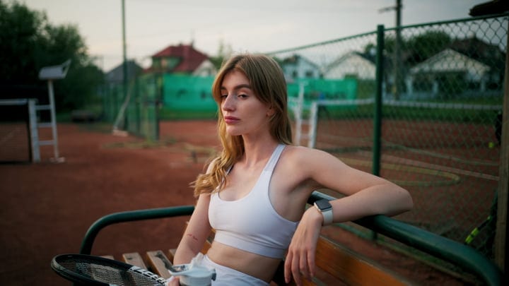 Female Tennis Player Resting On Bench At Clay Court