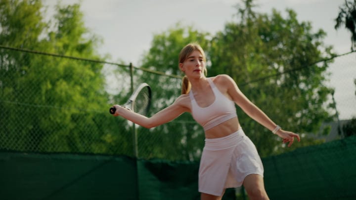 Focused Woman Playing Tennis Outdoors On A Sunny Green Court