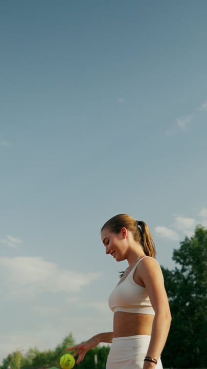 Young Woman Smiles While Preparing To Serve Tennis Ball On A Clay Court