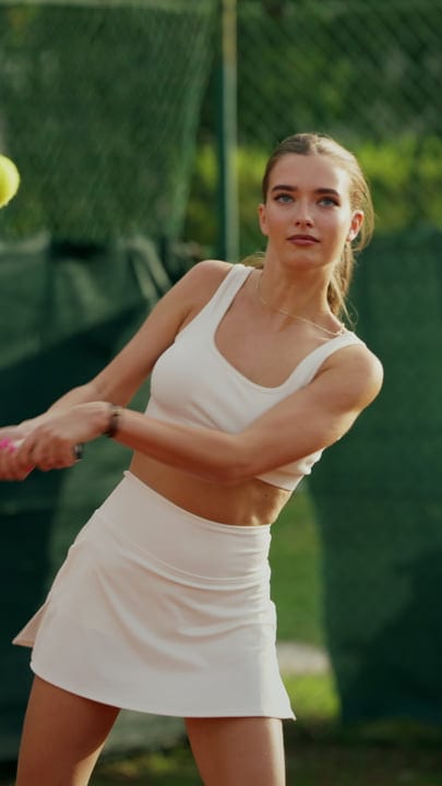 Young Woman In White Activewear Serving Tennis Ball On Clay Court