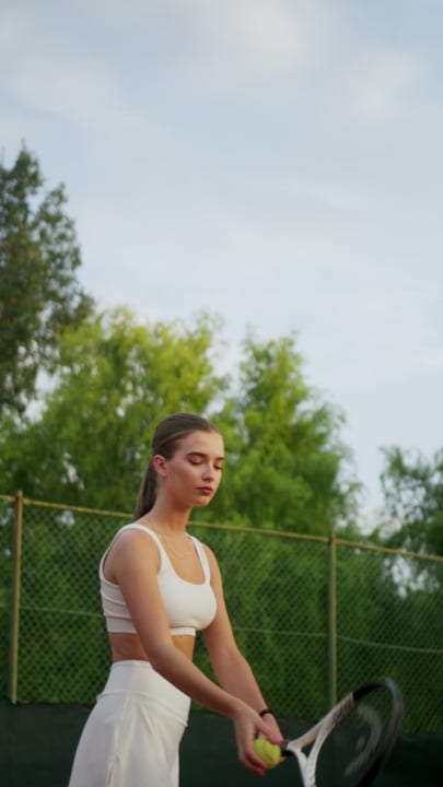 Young Woman Concentrates Before Serving Tennis Ball On Outdoor Court