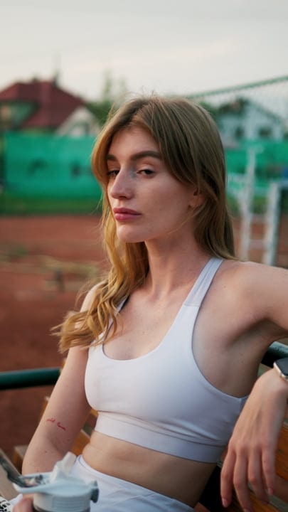 Young Woman Resting On A Bench At An Outdoor Tennis Court