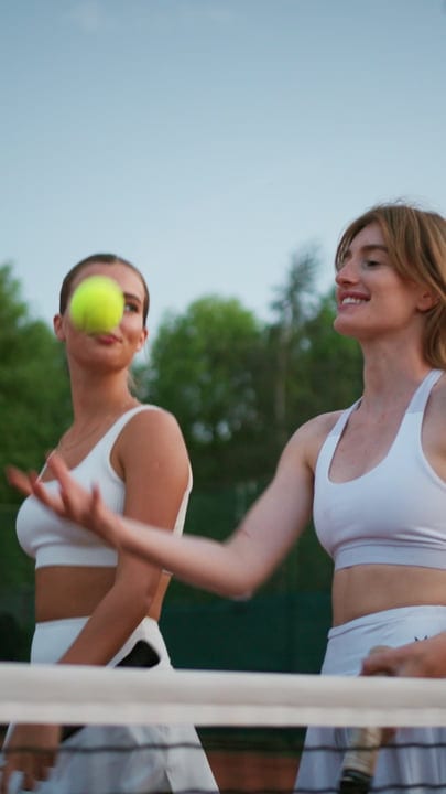 Two Women Playing Tennis, One Tossing Ball For Serve On Clay Court
