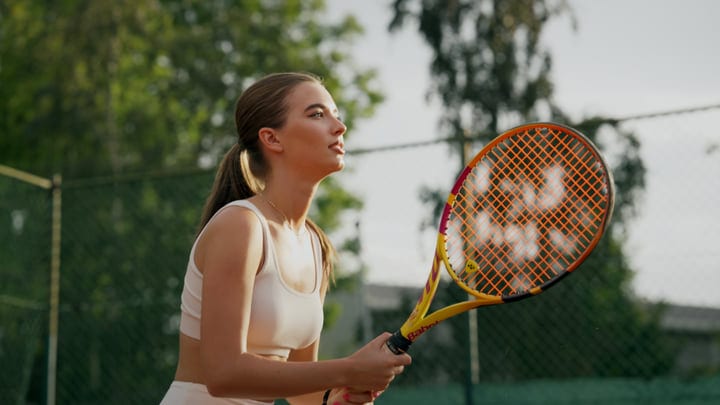 Young Woman Prepares To Serve During A Sunny Day On An Outdoor Tennis Court
