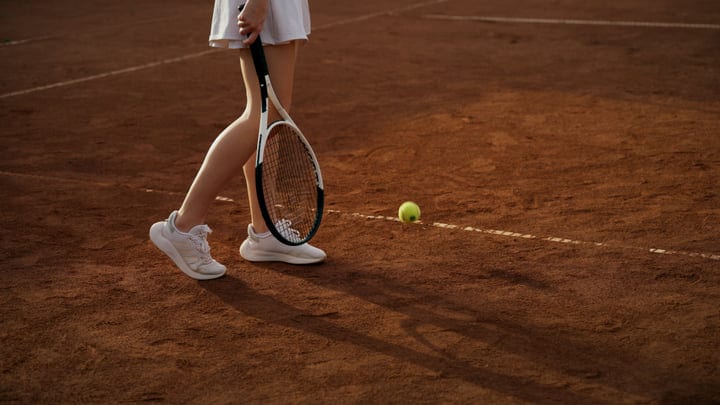 Female Tennis Player Walks On Clay Court With Racket And Ball