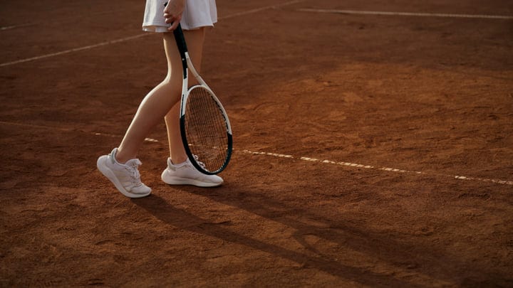 Female Tennis Player Standing On Clay Court With Racket
