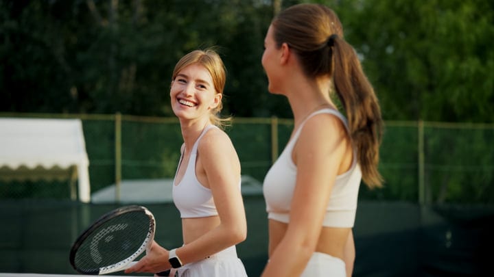 Happy Female Tennis Player Holding Racket On Outdoor Court With Partner