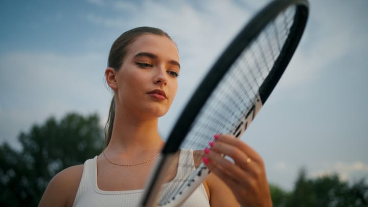 Young Female Tennis Player Examining Racket Strings Under Clear Sky