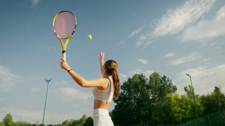Female Tennis Player Serves Ball On Outdoor Court Under Blue Sky