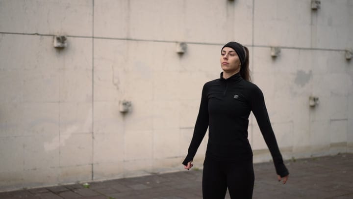 Focused Female Runner In Black Sportswear Pauses Against Concrete Wall