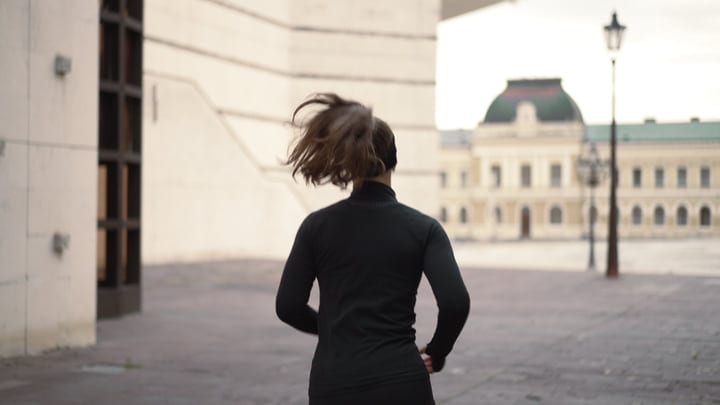 Woman Jogging In Dark Athletic Wear Through A European City Square