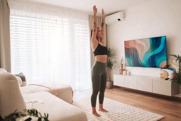 Woman Standing And Stretching Body Upwards In Bright Living Room