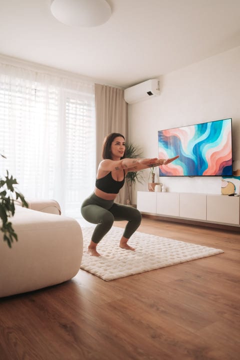 Young Woman Exercising With Squats In Her Bright Living Room At Home