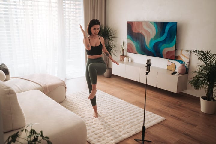 Young Woman Exercises Indoors Following Online Fitness Class On Phone