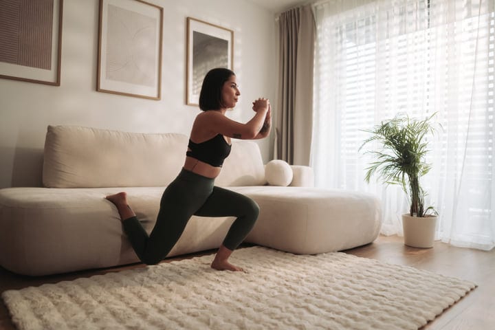 Young Woman Exercising Lunges On Rug In Her Modern Living Room