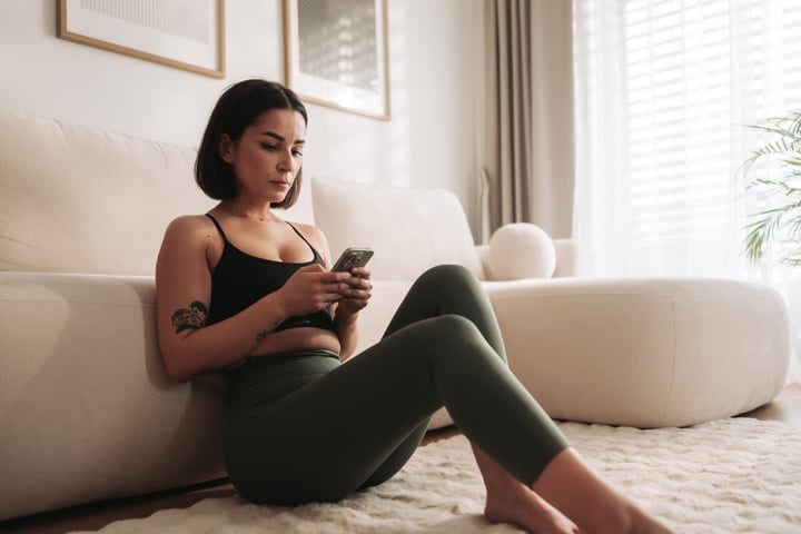 Young Woman Sitting On Floor Using Smartphone In Living Room