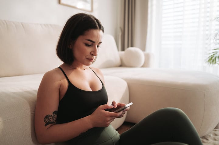 Young Woman Checking Phone On Floor In Bright Home Living Room