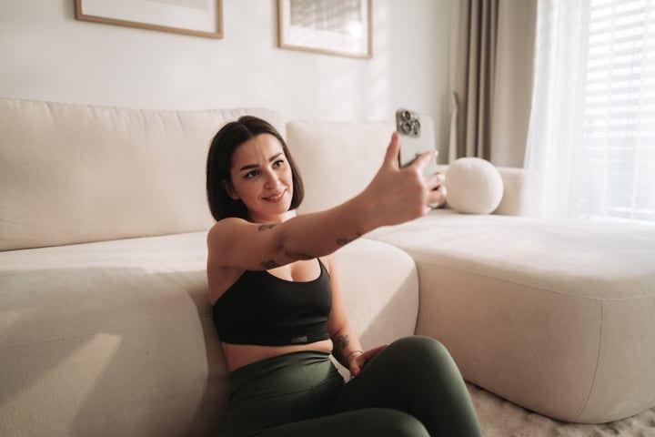 Young Woman Smiles Taking Selfie With Phone In Bright Living Room