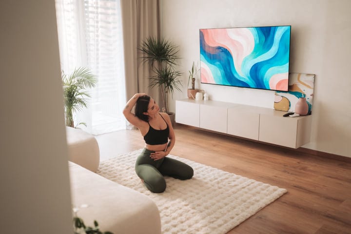 Young Woman Stretching Her Neck While Kneeling On Rug In Bright Living Room