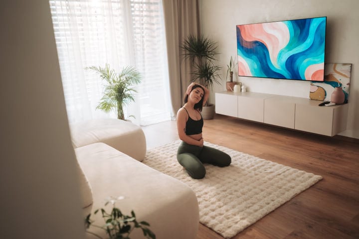 Young Woman Kneeling On Rug Stretching In Sunny Modern Living Room