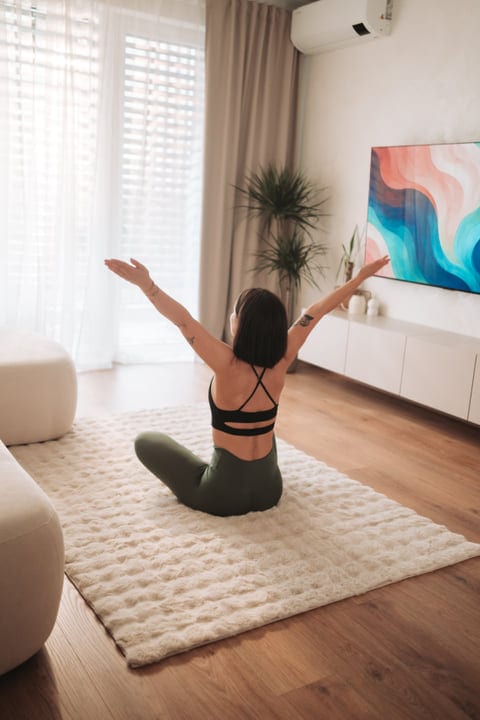 Woman Stretching Arms Upwards On Rug In Bright Living Room Morning