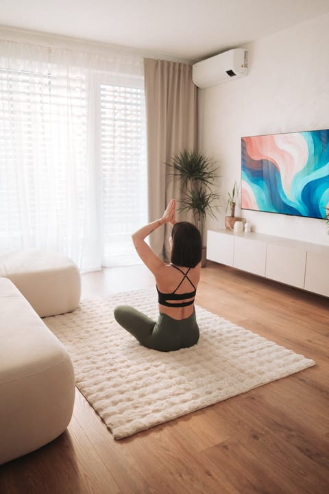 Woman Meditating On A White Rug In Her Bright Living Room At Home
